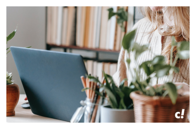 Eine teilweise sichtbare Frau arbeitet an einem Schreibtisch, der mit Laptop, Stiften und Pflanzen ausgestattet ist. Klimafreundlicher Onlinehandel