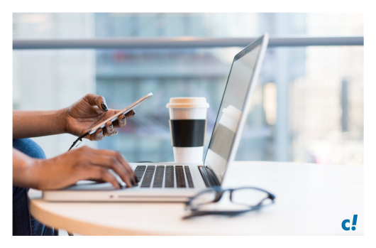 Eine Hand tippt auf einen Laptop und mit der anderen Hand wird ein Smartphone gehalten